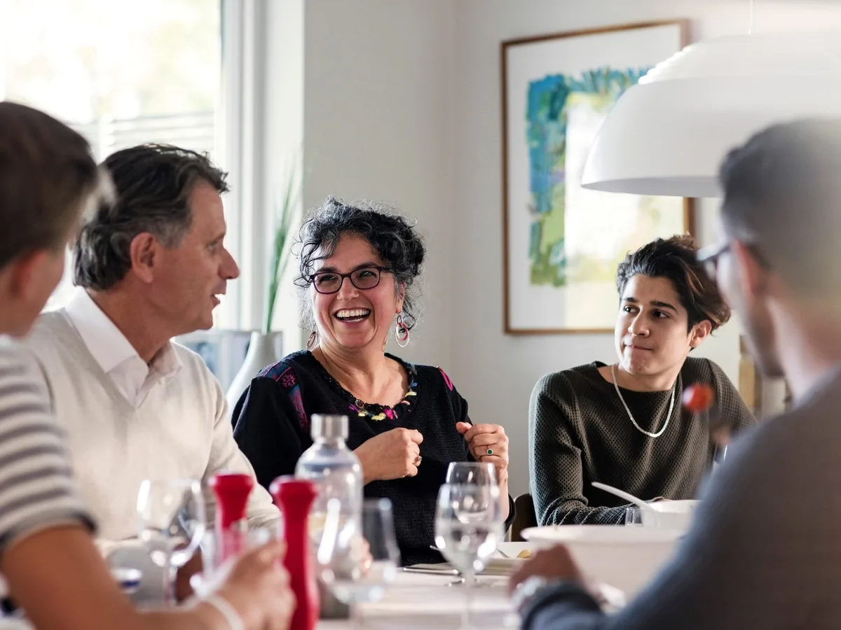 Repas de famille animé: une femme rit en pleine conversation autour de la table