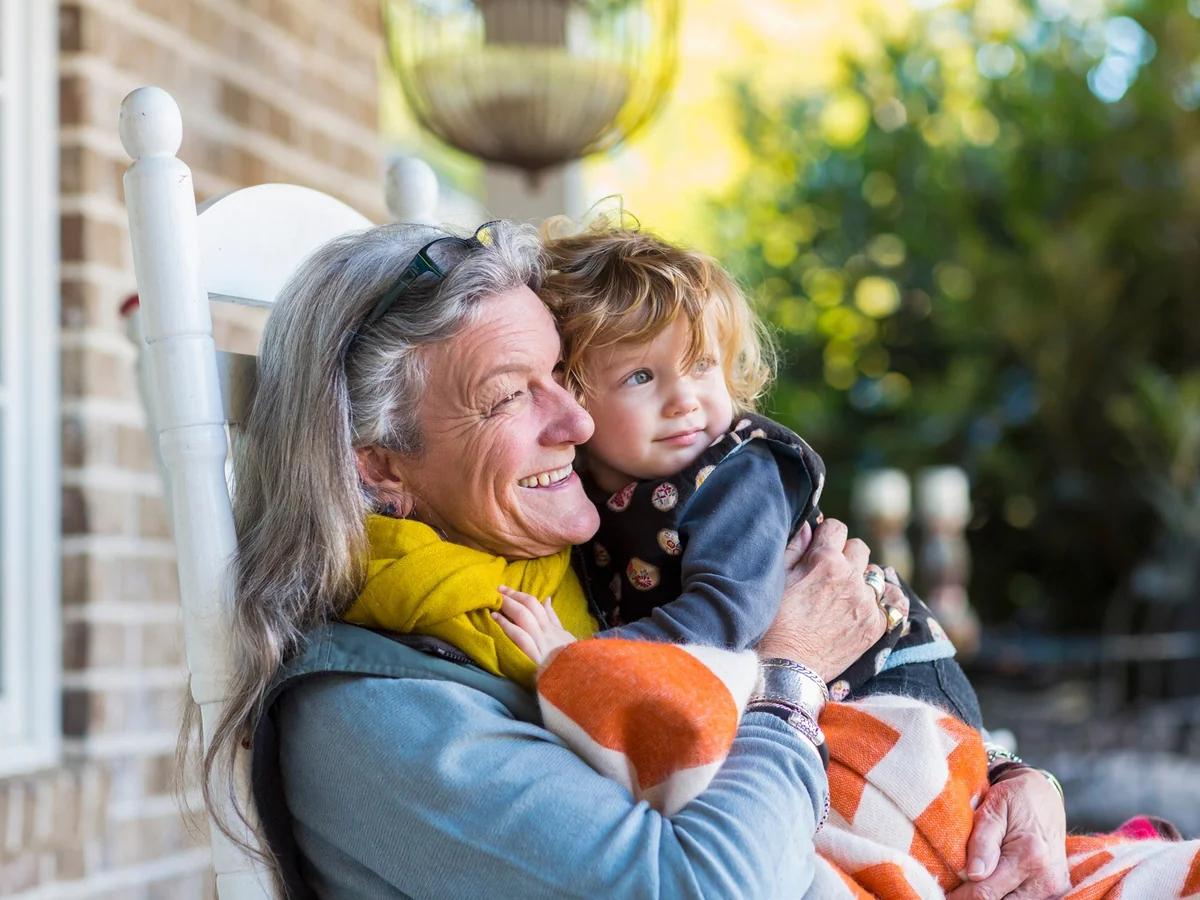 Grand-mère souriante tenant son petit-enfant sur une véranda ensoleillée