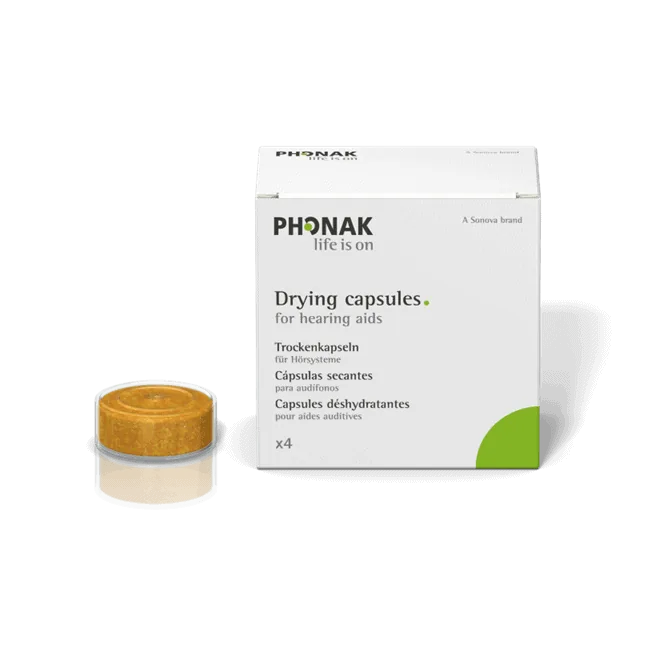 White cardboard box with the Phonak logo reading Drying capsules for hearing aids, with a round beige capsule set in front, on a black background.
